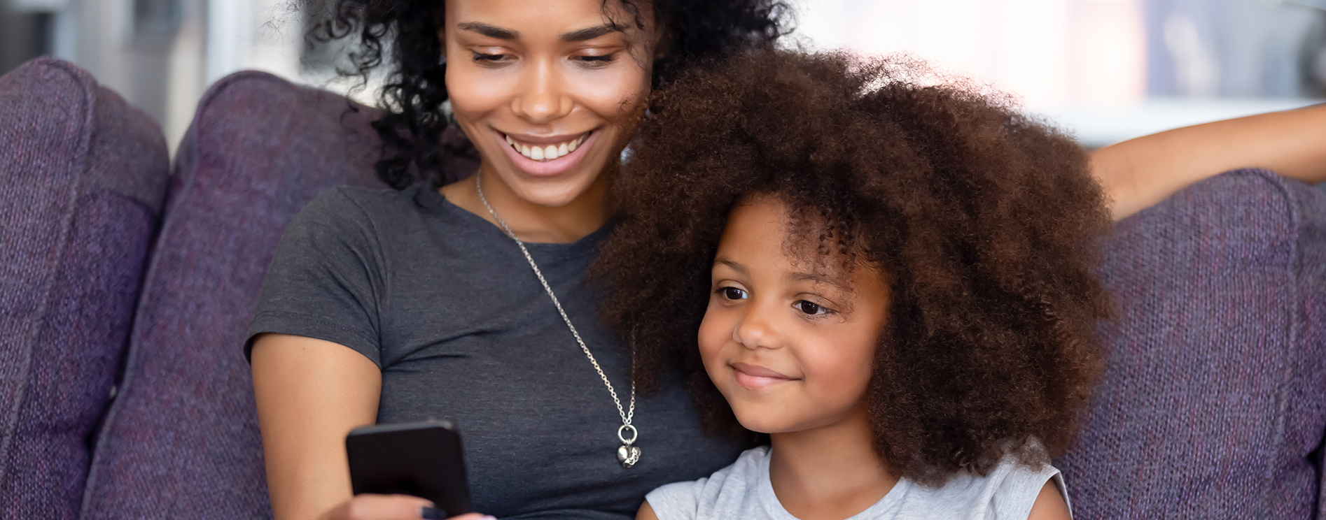 Cheerful mother little daughter spending time at home using smartphone Mother and daughter looking at their phone