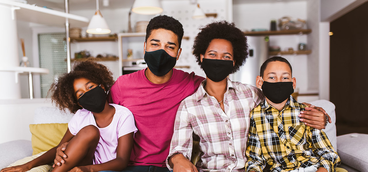 African American family sitting on a couch, wearing masks