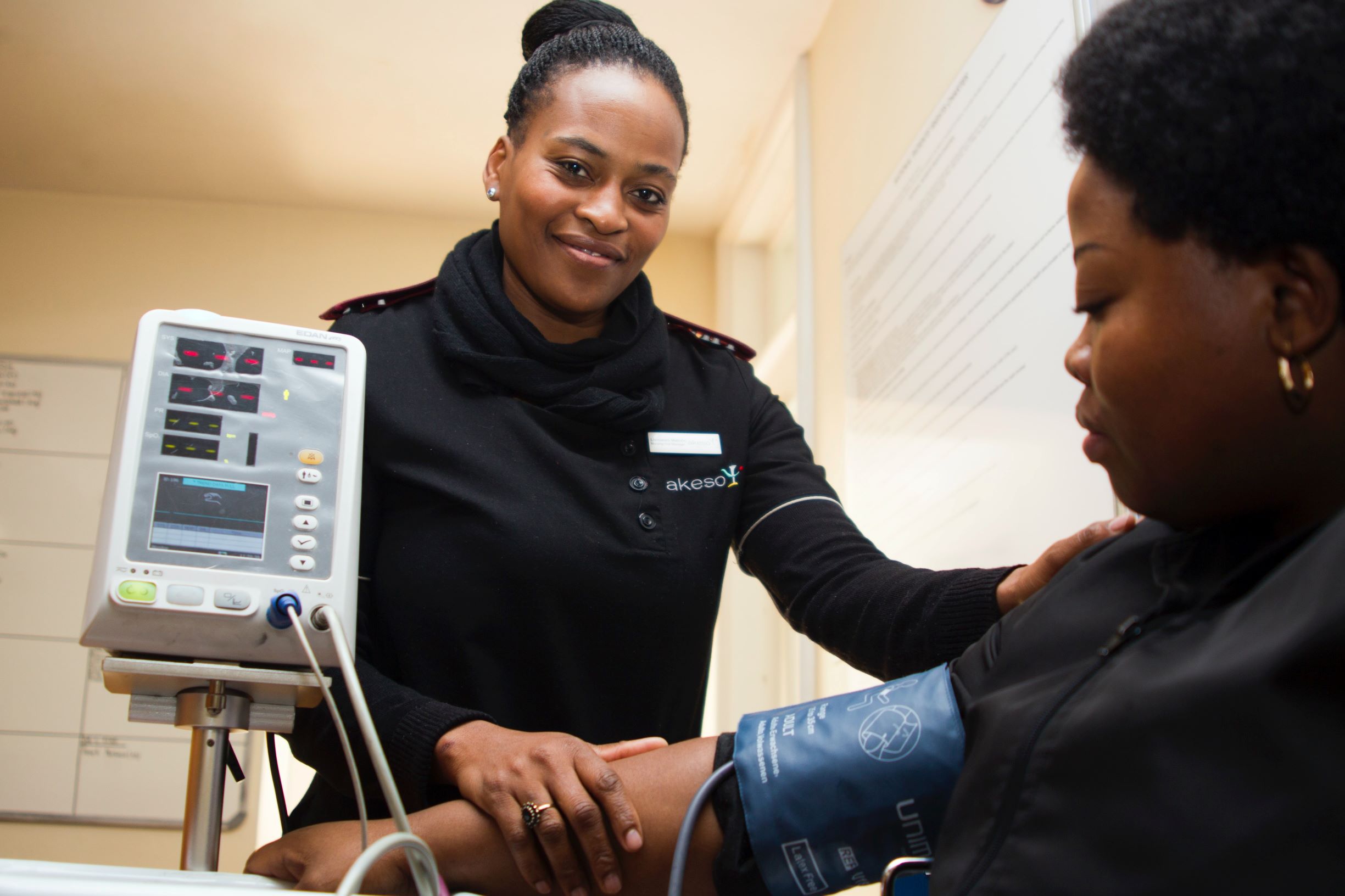 Nurse smiling and taking blood pressure of woman who is seated.