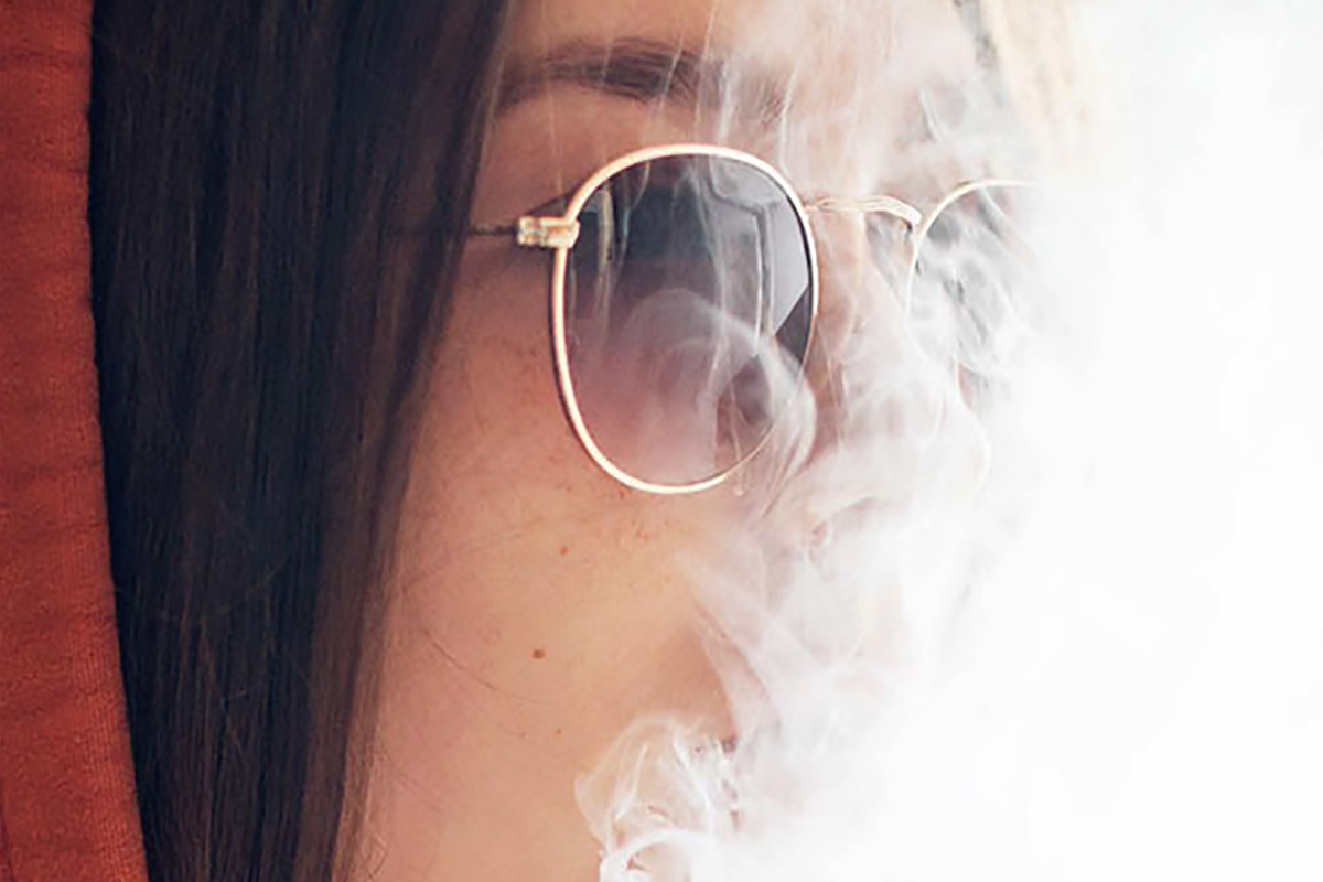 Mujer joven con gafas de sol con humo de vape