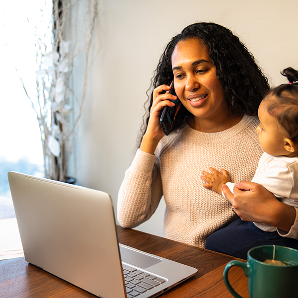 Mother holding child while on computer and phone