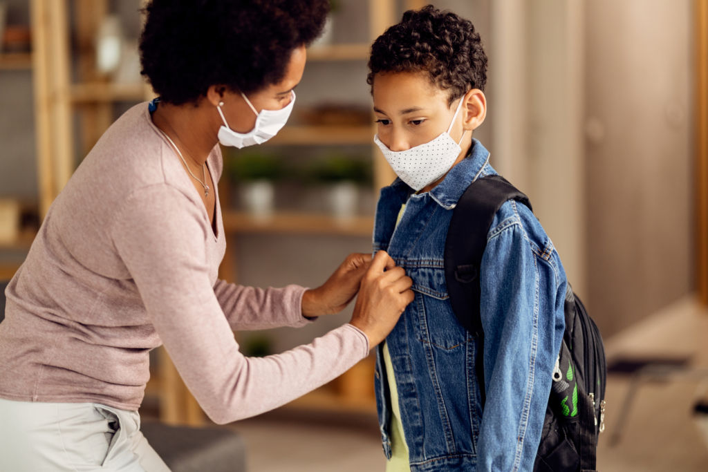 African American mom helps her son dress for school during coronavirus pandemic.