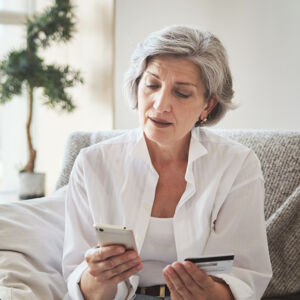 Elderly lady looking at smart phone and medical insurance card.