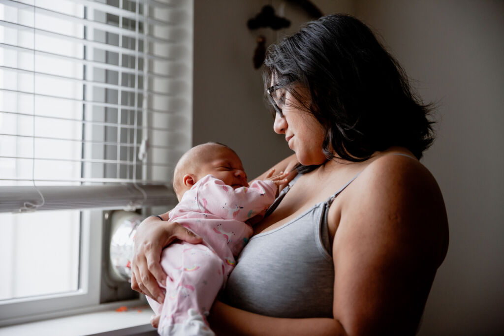 Mother and Newborn Baby Girl Standing Next to Bedroom Window