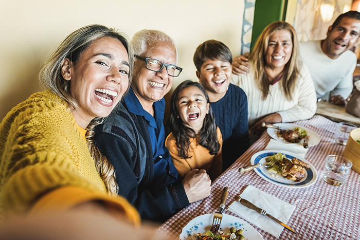 Multi-generational Hispanic family smiling and taking a selfie together at the dinner table. They are enjoying a healthy holiday meal and spend quality time.
