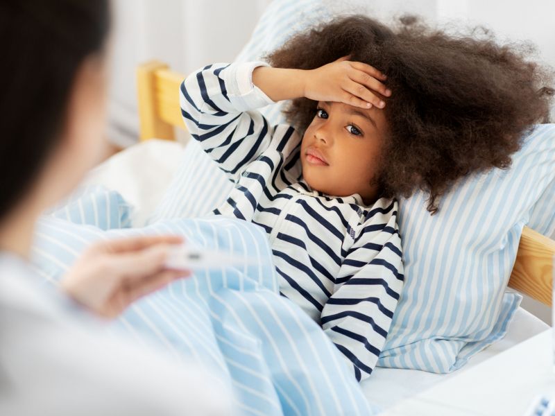healthcare, medicine and people concept - doctor with thermometer measuring temperature of little sick african american girl lying in bed at home